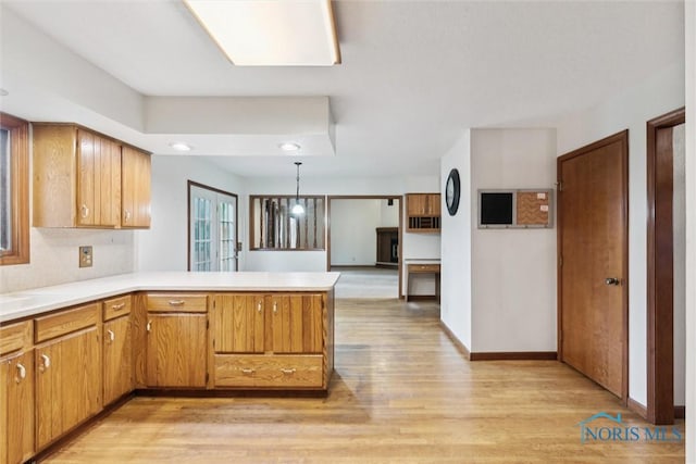 kitchen with light wood-style floors, a peninsula, light countertops, hanging light fixtures, and baseboards