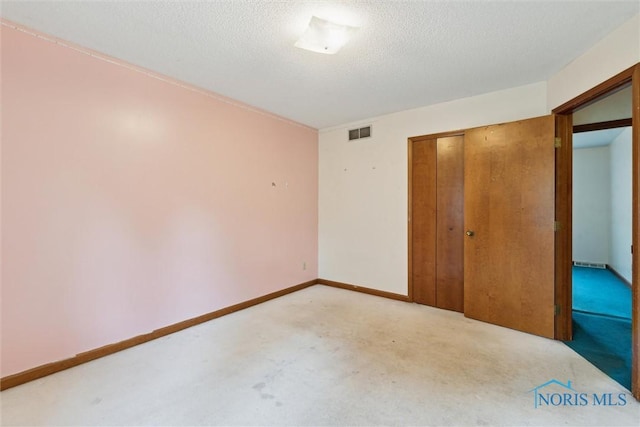 unfurnished bedroom featuring light colored carpet, a closet, a textured ceiling, and baseboards