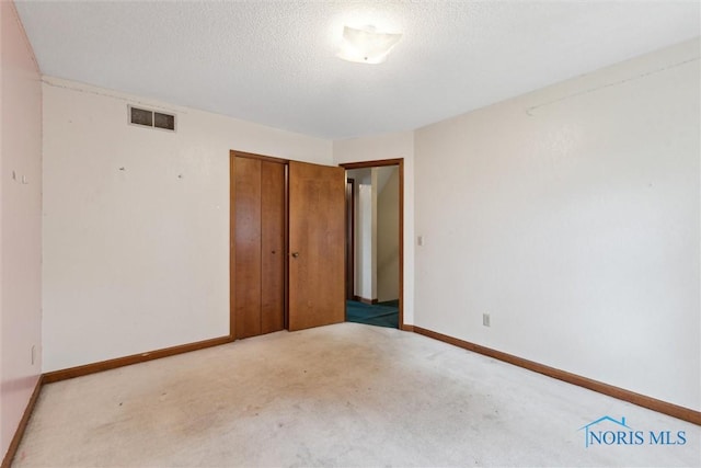 unfurnished bedroom with a closet, a textured ceiling, carpet flooring, and baseboards