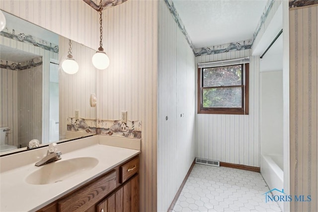 bathroom featuring wallpapered walls, baseboards, vanity, a bathtub, and toilet