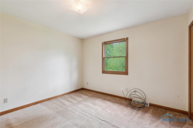 spare room with light colored carpet, baseboards, and a textured ceiling