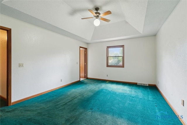 empty room with ceiling fan, a tray ceiling, carpet floors, and baseboards