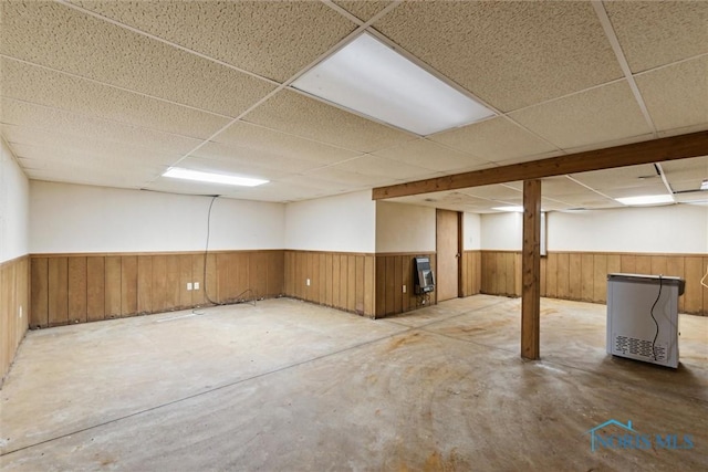 finished basement featuring wainscoting, a drop ceiling, and wooden walls