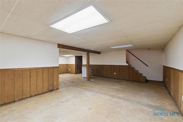 finished basement with a wainscoted wall, wood walls, a paneled ceiling, and stairway