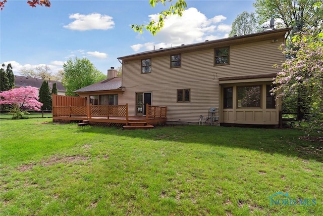 back of property featuring a deck, a chimney, and a yard