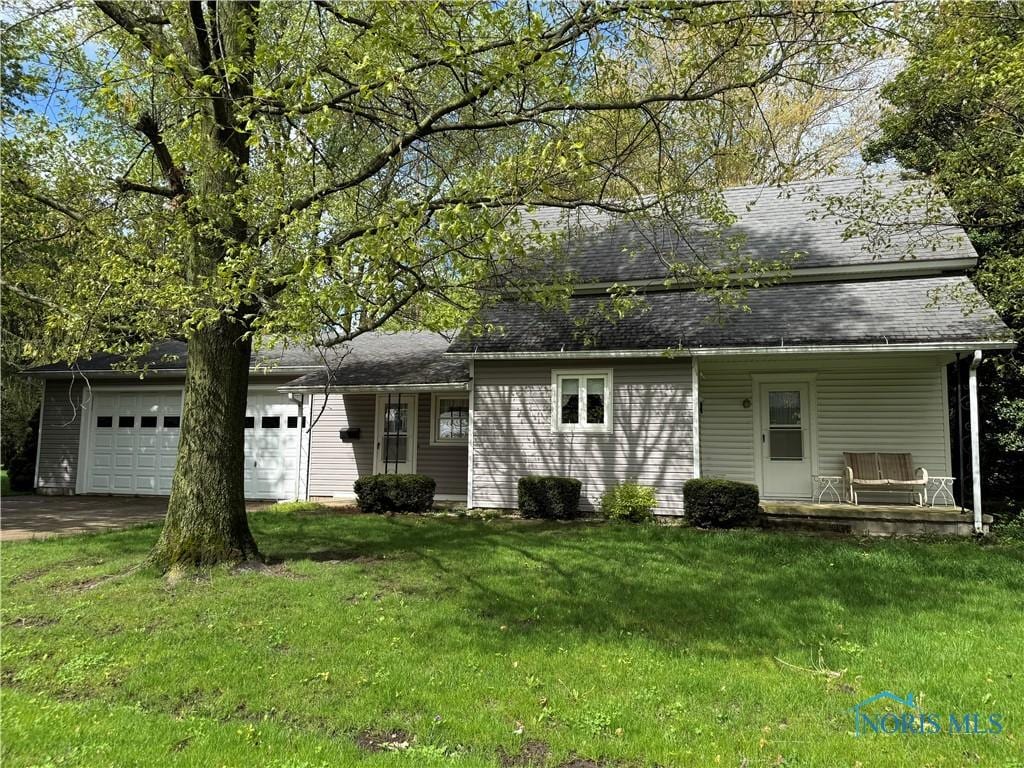 back of house with an attached garage, a porch, a lawn, asphalt driveway, and roof with shingles