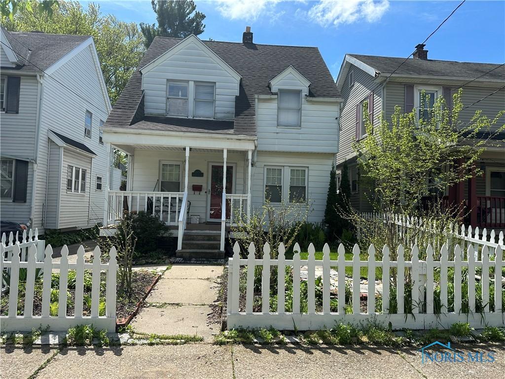 view of front facade featuring covered porch, a fenced front yard, and roof with shingles