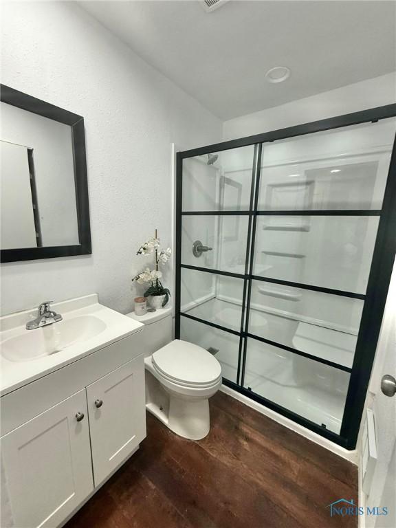 full bath with wood finished floors, a shower stall, vanity, and toilet