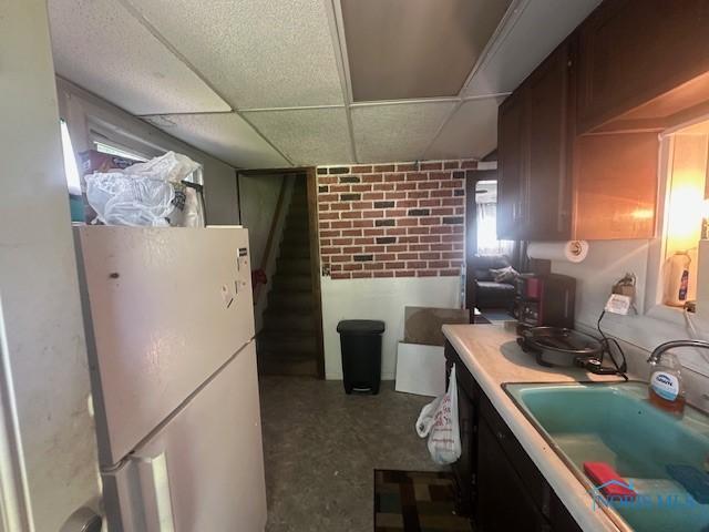 2111 Elm St, Toledo, OH 43608 - kitchen featuring freestanding refrigerator, a sink, a drop ceiling, brick wall, and light countertops