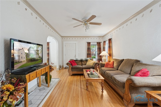 living room with a ceiling fan, light wood-style flooring, arched walkways, and ornamental molding