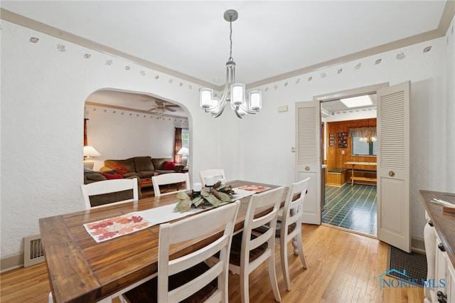 dining area with a chandelier, light wood finished floors, and arched walkways