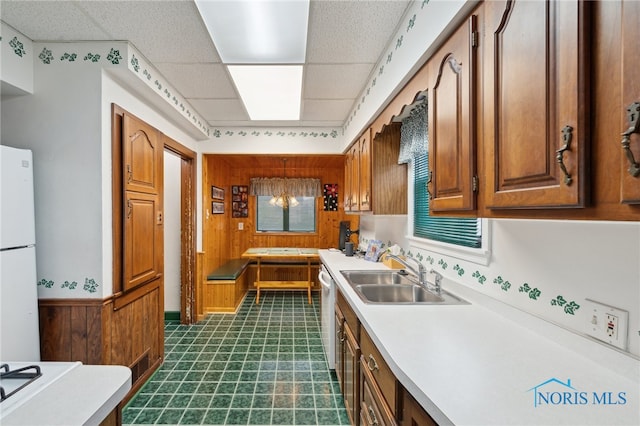 kitchen featuring a sink, dark flooring, light countertops, brown cabinetry, and white appliances