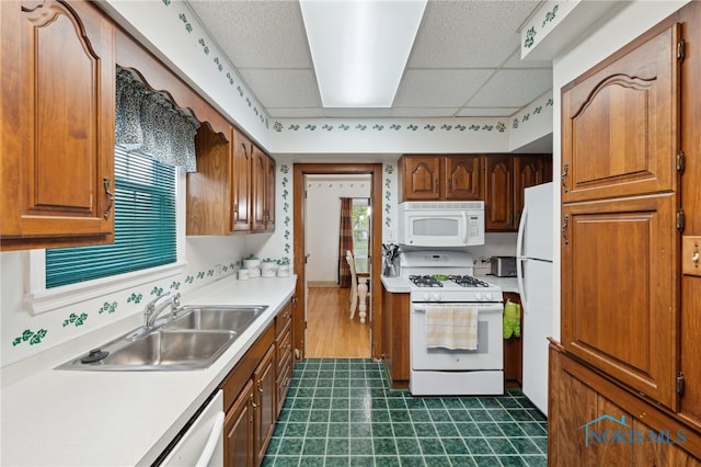 kitchen with white appliances, a sink, a paneled ceiling, dark flooring, and light countertops