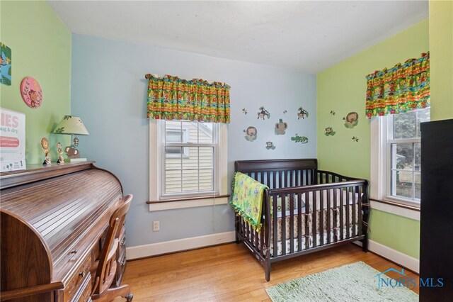 bedroom featuring wood finished floors, a crib, and baseboards