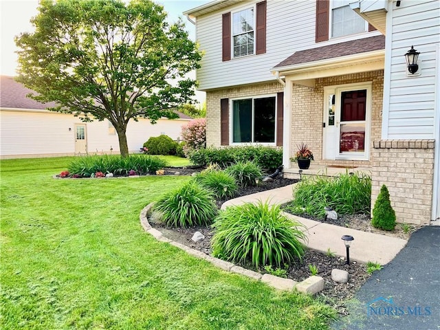 entrance to property with brick siding and a yard