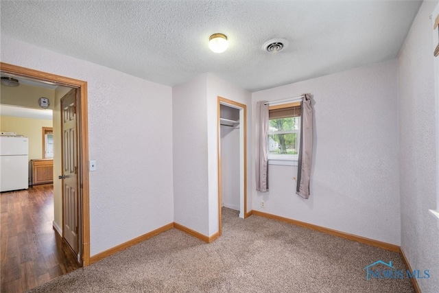 unfurnished bedroom featuring freestanding refrigerator, baseboards, a textured ceiling, a closet, and carpet