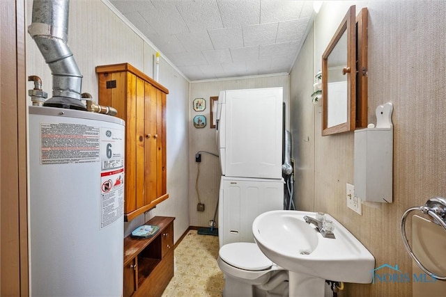 bathroom with water heater, stacked washer and clothes dryer, tile patterned floors, ornamental molding, and toilet