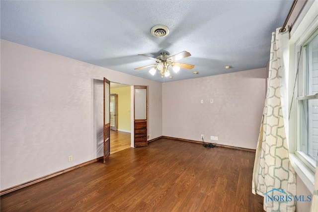 empty room featuring dark wood-style flooring, a ceiling fan, baseboards, and a textured ceiling