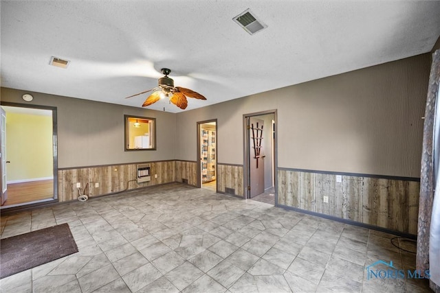empty room featuring wainscoting, ceiling fan, wood walls, a textured ceiling, and heating unit