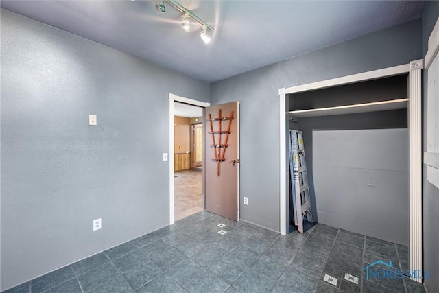 unfurnished bedroom with track lighting and dark tile patterned flooring