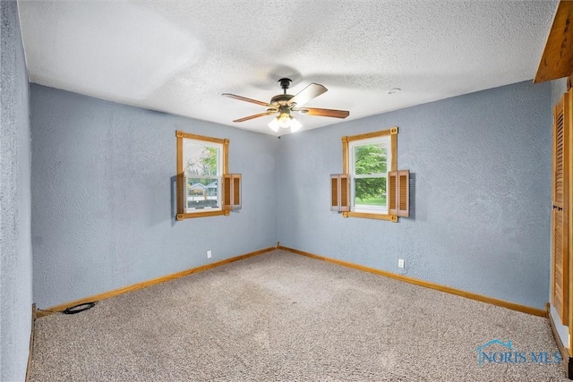 spare room with a textured wall, a ceiling fan, carpet floors, baseboards, and a textured ceiling