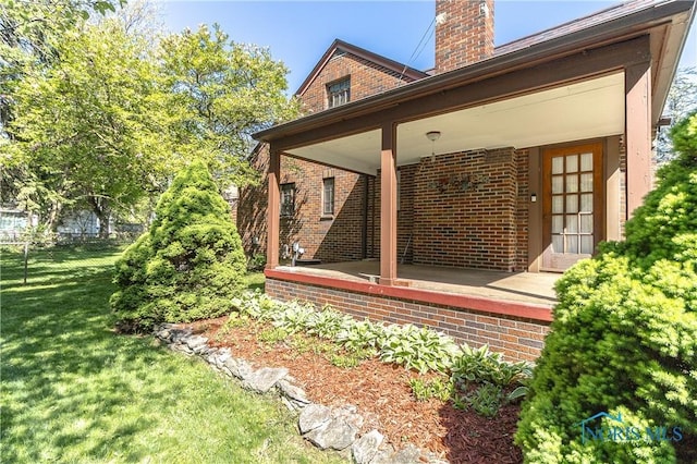 view of home's exterior featuring a chimney, brick siding, and covered porch