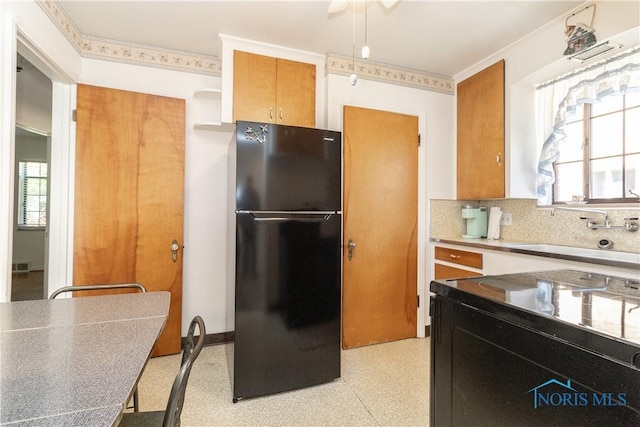 kitchen with freestanding refrigerator, a sink, plenty of natural light, light flooring, and crown molding
