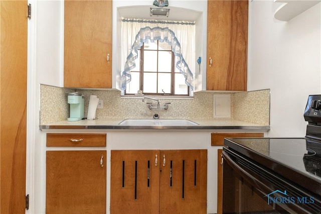 kitchen with black electric range oven, a sink, tasteful backsplash, light countertops, and brown cabinets