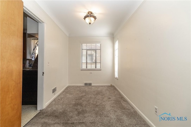 carpeted spare room featuring crown molding and baseboards