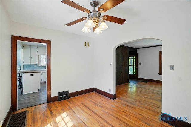 empty room featuring arched walkways, light wood finished floors, a ceiling fan, and baseboards
