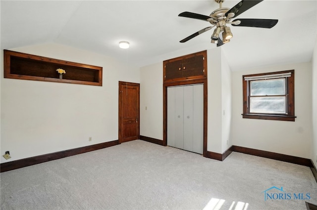 unfurnished bedroom featuring lofted ceiling, light carpet, baseboards, a closet, and ceiling fan
