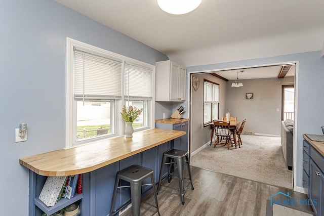 3134 Cragmoor Ave, Toledo, OH 43614 - kitchen featuring butcher block countertops, baseboards, a breakfast bar area, dark wood-style floors, and white cabinetry