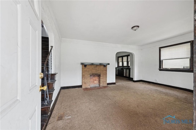 1908 Parkdale Ave, Toledo, OH 43607 - unfurnished living room with carpet floors, arched walkways, a brick fireplace, and baseboards
