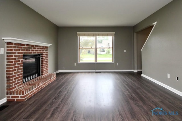 unfurnished living room featuring dark wood-style floors, baseboards, and a brick fireplace