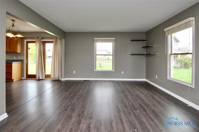 unfurnished living room featuring plenty of natural light, baseboards, and dark wood-style floors