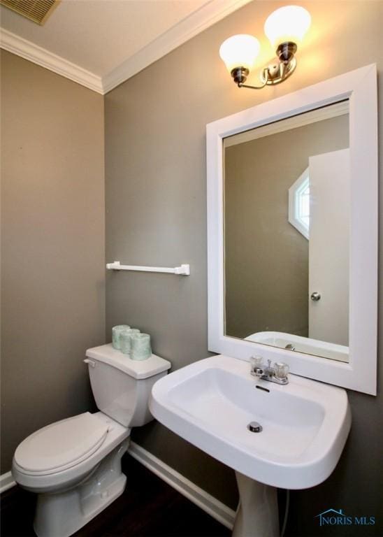 half bathroom featuring crown molding, toilet, baseboards, and a sink