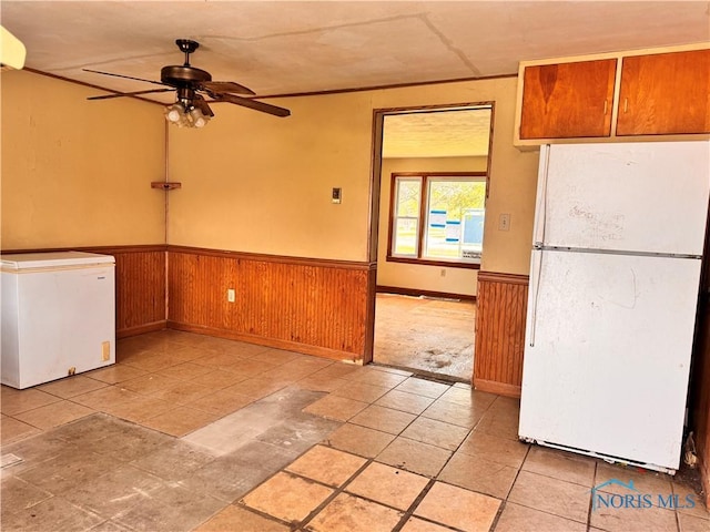 unfurnished dining area with wainscoting, ceiling fan, and wood walls