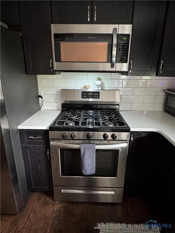 kitchen with appliances with stainless steel finishes, dark cabinetry, dark wood-style flooring, light countertops, and backsplash