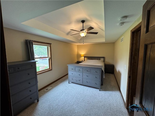 bedroom with a tray ceiling, light colored carpet, baseboards, and ceiling fan