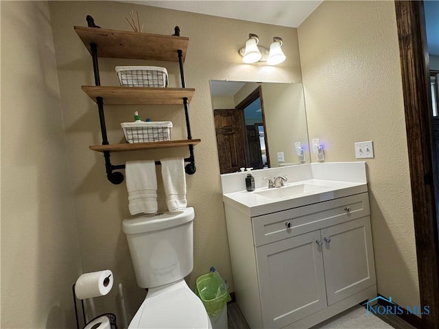 bathroom featuring toilet, vanity, and a textured wall