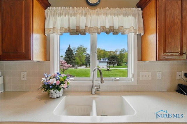 29030 Hufford Rd, Perrysburg, OH 43551 - kitchen featuring a sink, light countertops, brown cabinetry, and backsplash