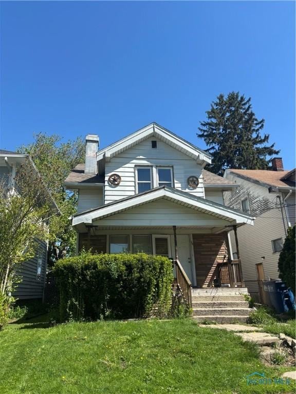 view of front of property with a front yard, a chimney, and covered porch