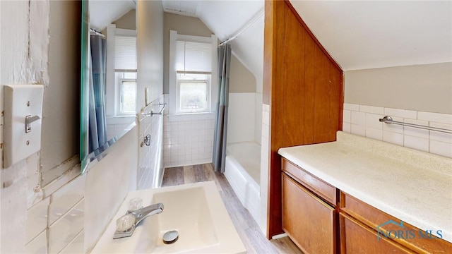 full bath with vaulted ceiling, tile walls, wood finished floors, and vanity