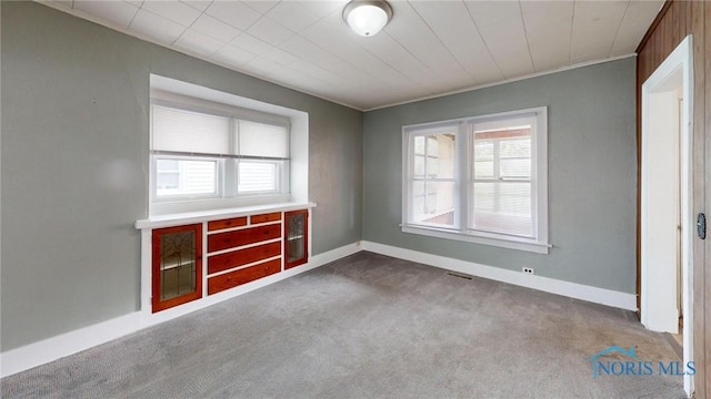 carpeted empty room with healthy amount of natural light, baseboards, and ornamental molding