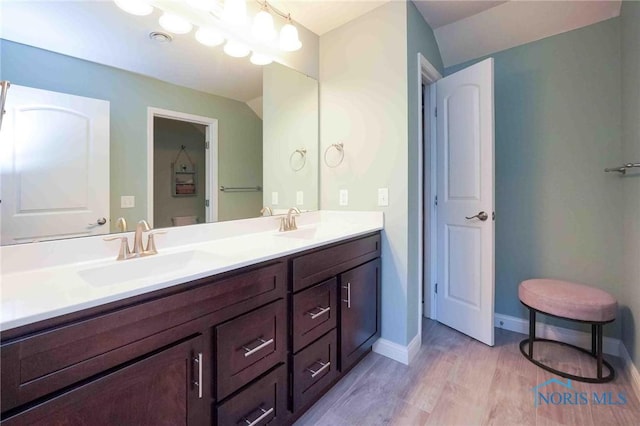 full bath featuring wood finished floors, double vanity, and baseboards