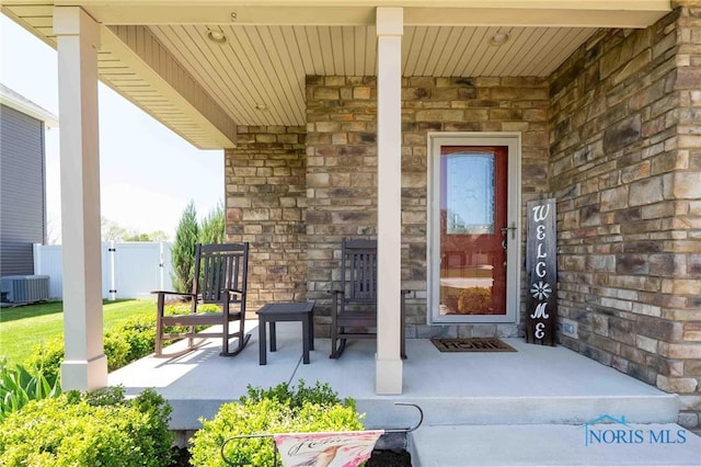 entrance to property featuring central air condition unit, stone siding, a porch, and fence