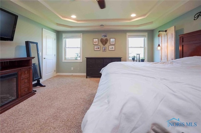 bedroom with a raised ceiling, multiple windows, light carpet, a fireplace, and recessed lighting