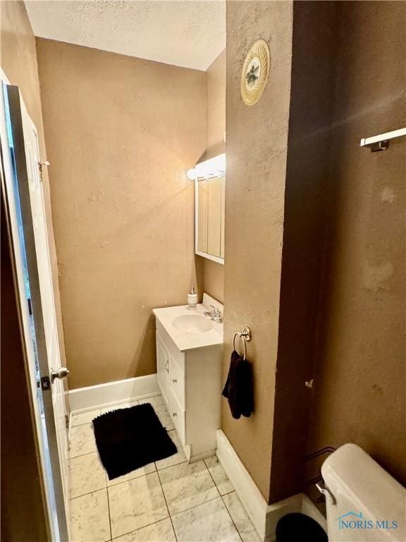 bathroom featuring toilet, a textured ceiling, baseboards, and vanity