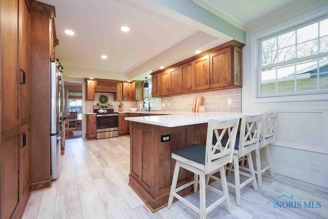 2057 Windsor Pl, Findlay, OH 45840 - kitchen featuring stainless steel appliances, a peninsula, brown cabinetry, decorative backsplash, and light wood-style flooring
