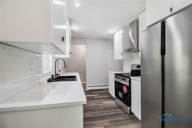 kitchen featuring stainless steel appliances, wall chimney exhaust hood, a baseboard radiator, a sink, and ventilation hood